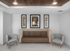 Modern seating area with a brown couch flanked by two gray chairs. Three framed art pieces hang on the wall above, set against a white background.