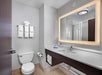 Modern bathroom with a toilet, towel rack, illuminated mirror, and sink. Towels and toiletries are neatly arranged. Neutral color palette with a focus on clean design.