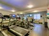 A modern gym with treadmills, an elliptical machine, and exercise bikes facing mirrors and TVs. The room has wooden flooring and bright lighting.