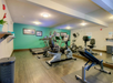 A gym room with exercise bikes, treadmills, and a weight bench. Mirrors cover one wall, and framed pictures hang on the opposite teal wall.