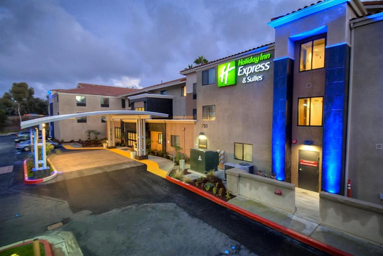 Exterior view of a Holiday Inn Express & Suites at dusk, featuring illuminated signage and a covered entrance.