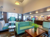 Hotel lobby with turquoise seating, wooden tables, and pendant lighting. The space includes a breakfast area with food displays in the background.