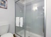 A modern bathroom features a glass-enclosed shower with two white towels on the door, a toilet to the left, a framed picture on the wall, and a wall light fixture.