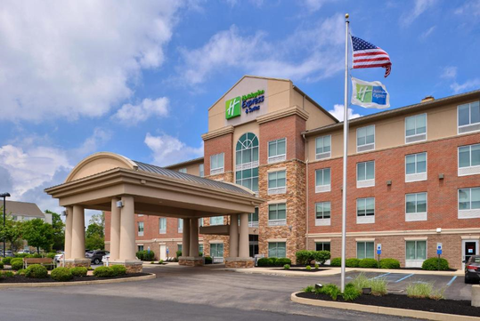 Four-story hotel with red brick exterior, featuring a covered entrance and an American flag flying on a pole. The sky is partly cloudy.