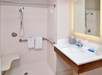 Accessible bathroom with a walk-in shower, grab bar, folding seat, single vanity sink, and mirror. White towels hang from the grab bar.