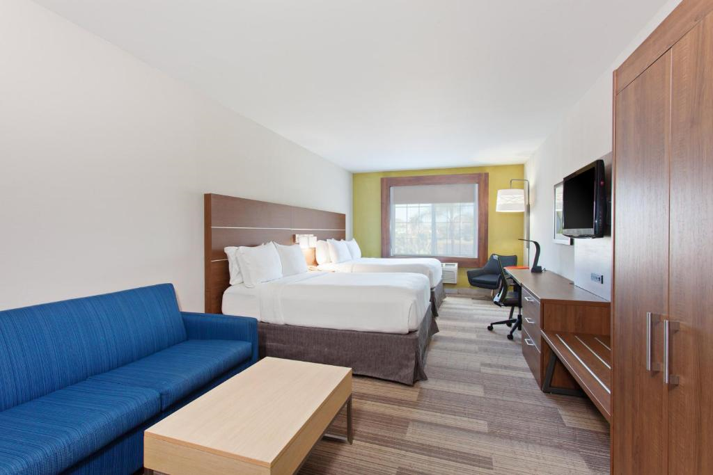 Hotel room with two double beds, a blue sofa, wooden desk with TV, and a window with natural light.