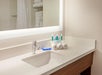 Bathroom countertop with a sink, illuminated mirror, rolled white towels, and toiletries including bottles and soap.