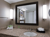 A bathroom with a granite countertop, sink, tissue box, toiletries, and towels. A large mirror is above the sink, flanked by two lights. A framed artwork is reflected in the mirror.