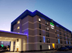 A four-story hotel building with blue neon lighting at dusk, featuring a brightly lit entrance area.