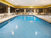 Indoor swimming pool surrounded by lounge chairs and large windows.