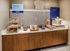 Breakfast station with pastries, bread, and a toaster on a wooden counter beneath decorative bakery signs.