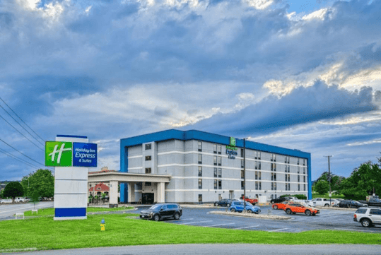 Exterior view of a Holiday Inn Express & Suites hotel with parked cars and a cloudy sky in the background.