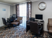 Hotel business center with two computer desks, chairs, a printer, and a wall clock. Office-style decor with patterned carpet and sheer curtains.