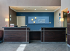 Hotel front desk with a dark wood counter, a blue wall, and a Holiday Inn Express logo. Lamps are on each side, and there is a chair in the left corner.