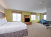 Spacious hotel room with a large bed, flat-screen TV, blue sofa, and green accent wall near two windows.