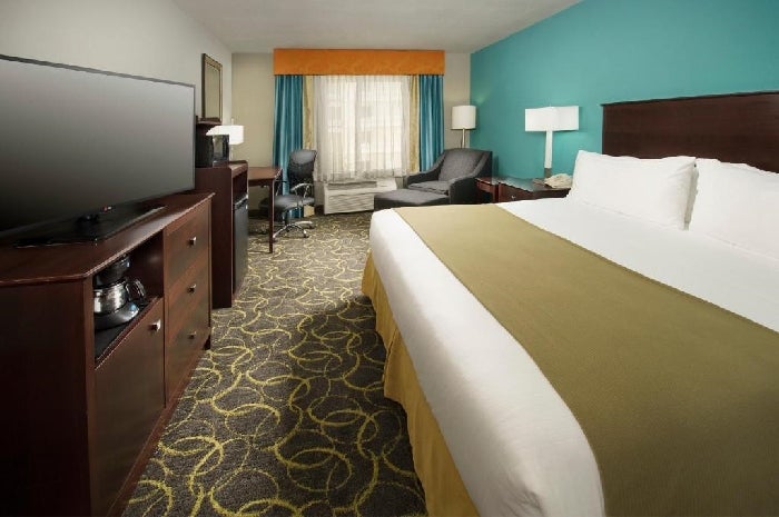 One king bed, armchair, work desk and a flat-screen TV inside a guest room.