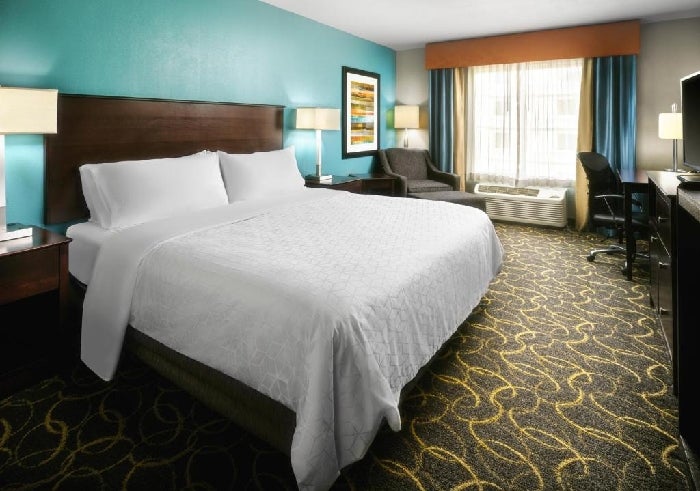 One king bed, armchair, work desk and a flat-screen TV inside a guest room.