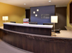 Front desk of a Holiday Inn Express lobby with a curved counter, three chairs, lamps, and a sign on the wall.