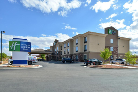 Exterior view of a Holiday Inn Express & Suites hotel with parking lot, cars, and a sign under a partly cloudy sky.