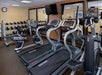 A gym with treadmills, a recumbent bike, wall mirrors, weights on a rack, and two wall clocks above.