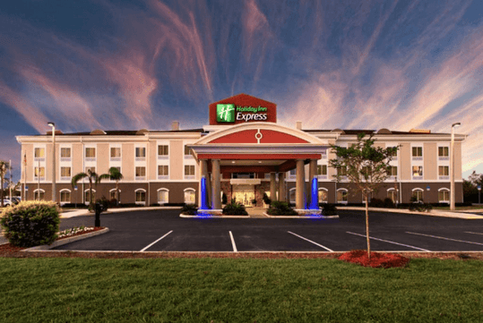 Front view of a Holiday Inn Express hotel with a lit entrance and parking lot at sunset.