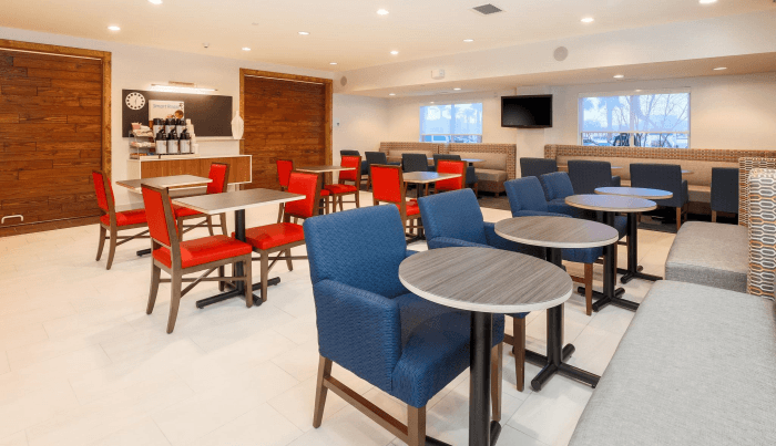 A dining room with square tables with red chairs, and round tables with cushioned benches on one side and blue chairs on the other.