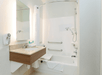 A small modern bathroom with a small sink with a lit mirror over it and an accessible shower and tub combo with several grab bars and a bench.