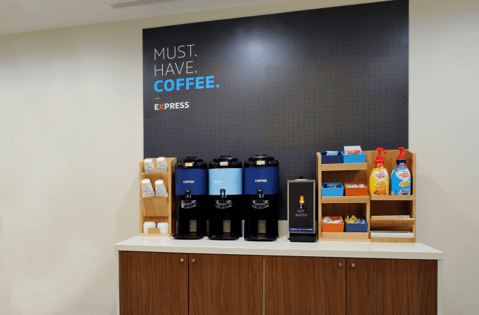 A coffee bar with cup and coffee dispensers on the left and several types of creamers on the right.