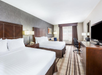 Hotel room with two double beds, a desk, chair, and TV. The room has striped carpet and a large window with curtains.