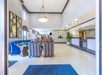 Hotel lobby with modern decor, featuring colorful chairs, a large reception desk, plants, and artwork on the walls. Bright lighting and tiled floors.