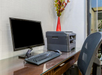 A modern office desk setup features a computer monitor, keyboard, mouse, and a multifunction printer. A red vase with flowers is placed on the desk.
