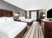 Hotel room with two double beds, white linens, a patterned carpet, a large window, dark wood furnishings, a desk, chair, and flat-screen TV.