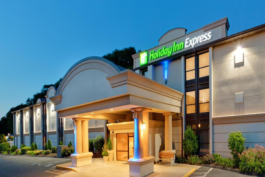 Exterior view of a Holiday Inn Express with a well-lit entrance and surrounding greenery at dusk.