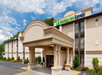 Exterior of a Holiday Inn Express with beige walls, large entrance, and green signage against a cloudy sky.