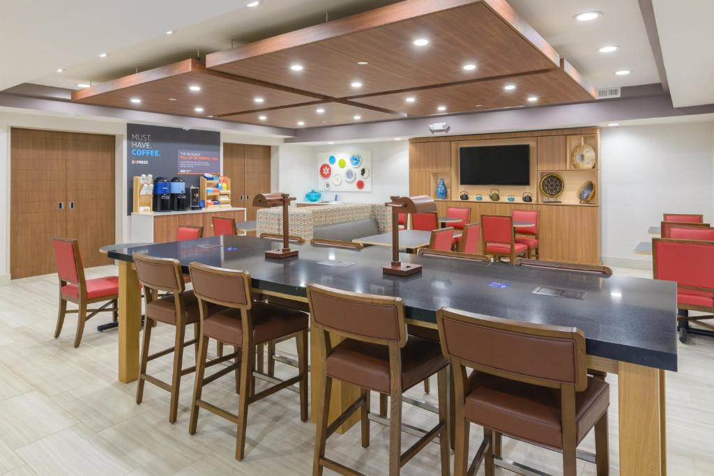 Modern community space featuring a long table with chairs, wall-mounted TV, red seating area, and a coffee station.