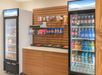 Snack shop with two refrigerated display cases containing drinks and sandwiches, and a wall shelf with chips and candy.