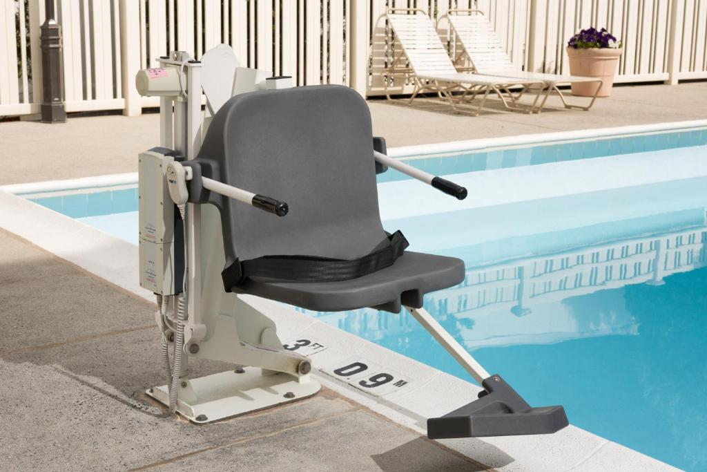 A gray pool lift chair is positioned next to a pool with the water's edge marked at 3 feet 9 inches. White lounge chairs and a potted plant are in the background.