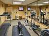 A small gym with treadmills, a stationary bike, an elliptical, and a bench. Mirrors cover one wall, and a TV is mounted overhead.