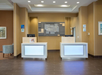 Hotel reception area with two modern check-in desks, a decorative wall panel, signage, and seating area to the left.