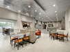 A modern, spacious hotel lobby with seating areas, tables, and a coffee station, featuring neutral tones and contemporary decor.