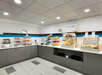 Self-serve breakfast area with pastries, bread, a coffee machine, and display cases on a countertop in a modern setting.