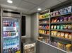 A small convenience store with beverages in two refrigerated units and shelves stocked with various snacks, chips, and candy bars.