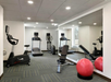 A gym room with cardio machines, a weight bench, a red exercise ball, and a large mirror on the wall.