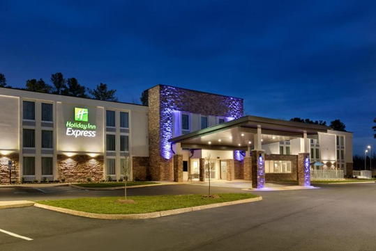 Holiday Inn Express building at dusk with illuminated entrance and signage, surrounded by trees and a parking lot.