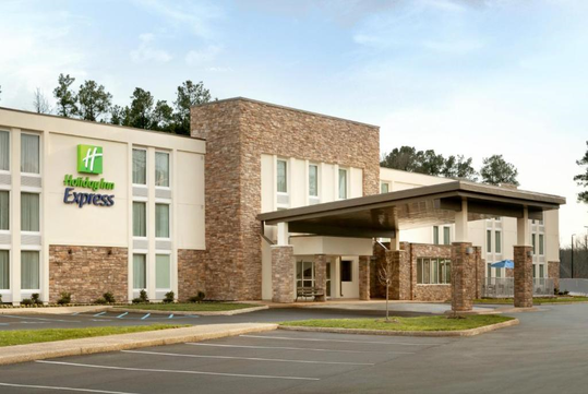 Exterior of a Holiday Inn Express hotel with a brick facade, large windows, and an entrance canopy, surrounded by trees.