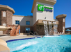 Outdoor pool with waterfalls at a Holiday Inn Express, featuring stone accents, blue water, and lounge chairs under a clear sky.
