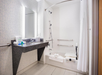 Accessible bathroom with a bathtub, shower curtain, grab bars, and a wall-mounted sink. Towels and toiletries are on the sink and bathtub edge.