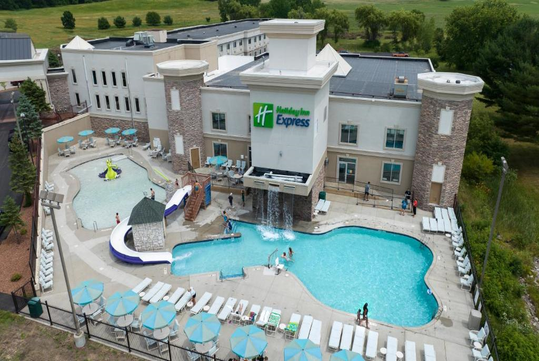 Aerial view of a Holiday Inn Express hotel with an outdoor pool area featuring a slide and seating, surrounded by greenery.