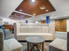 Modern hotel lobby with a beige sofa, gray coffee table, and patterned armchairs. Wooden ceiling panels and a blend of blue and brown decor create a welcoming atmosphere.