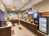 Breakfast buffet in a modern hotel dining area, featuring yogurt, eggs, milk, cereals, and beverages. Warm lighting and wooden decor create a welcoming atmosphere.